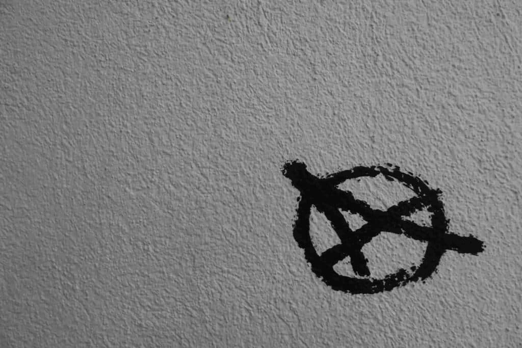 The anarchist symbol painted in black on a white surface. Online counselling and therapy with William Smith.