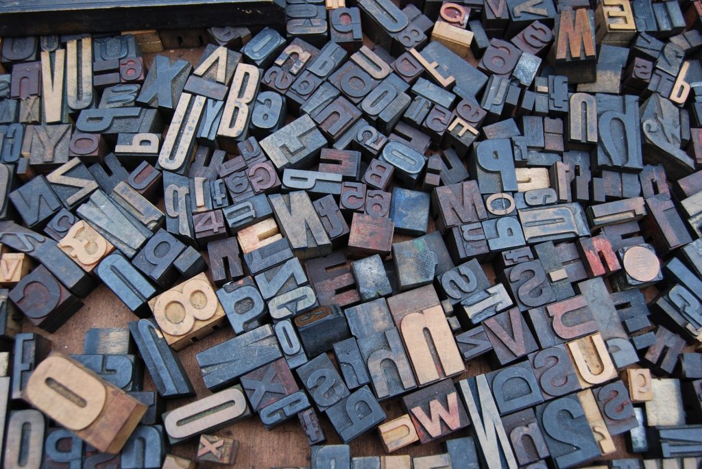 A jumble of wooden typeset letters and numbers spread out across a wooden board, to represent the confusing array of abbreviations used in counselling and psychotherapy