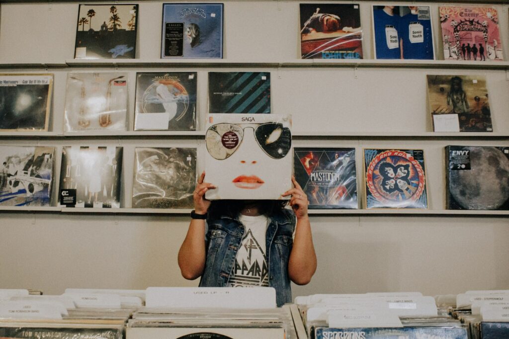 Person in record shop holding album cover to hide their face. 
