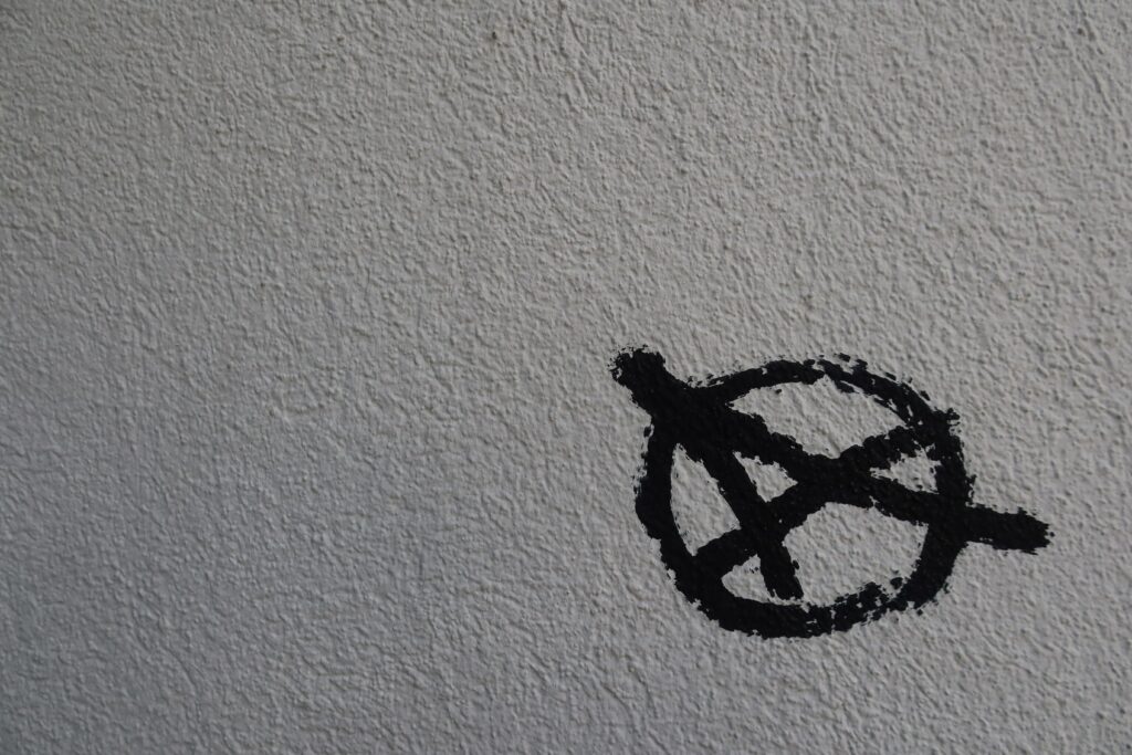 The anarchist symbol painted in black on a white surface. Online counselling and therapy with William Smith.