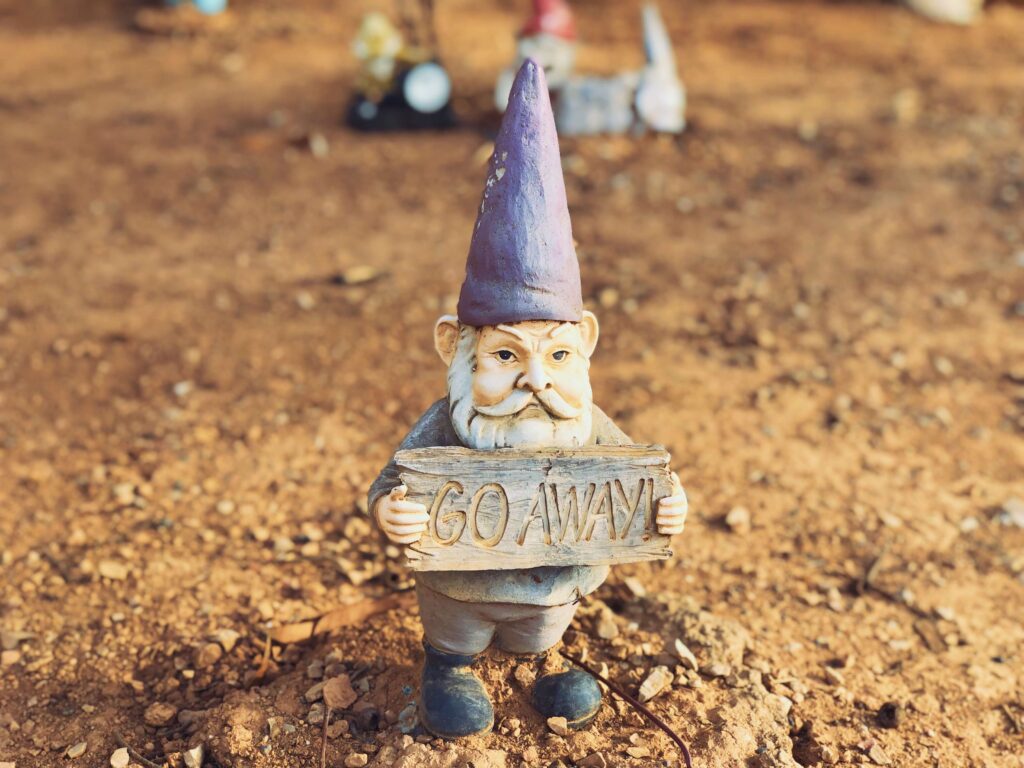 A garden gnome wearing a purple pointy hat holding a sign that reads "GO AWAY". Discrimination and prejudice can be a part of culture shock.
