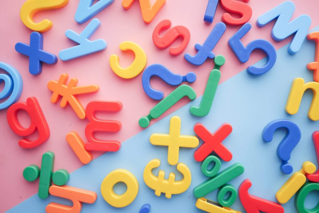 Colourful plastic letters, numbers and symbols are randomly arranged on a board that is half pink and half blue. Language barrier can be a part of culture shock.