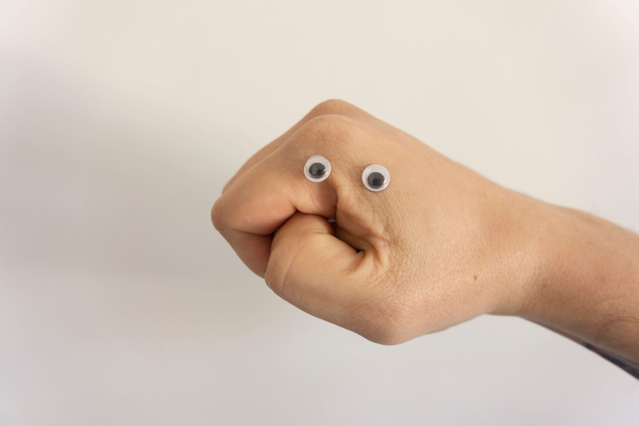 A hand in the shape of a fist. Two plastic googly eyes have been stuck on the side of the knuckled so that the fist resembled a face.