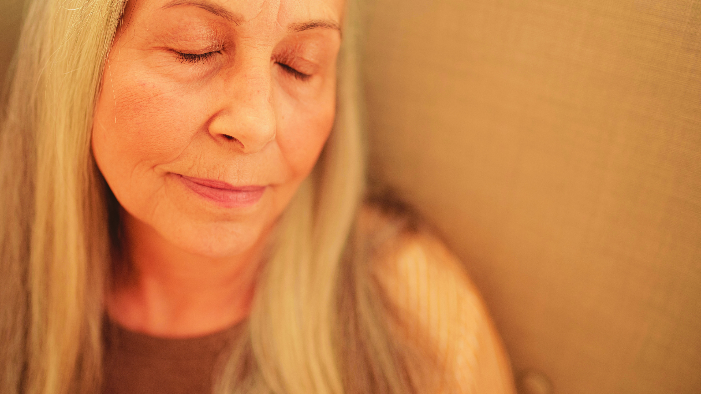 Person with grey long hair and eyes closed is gently smiling