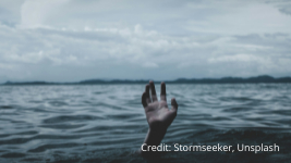 therapist drowning due to burnout A single hand reaches out of the water in a large body of water under a cloudy sky, suggesting a person struggling or calling for help. Distant shoreline is visible in the background. Credit: Stormseeker, Unsplash.